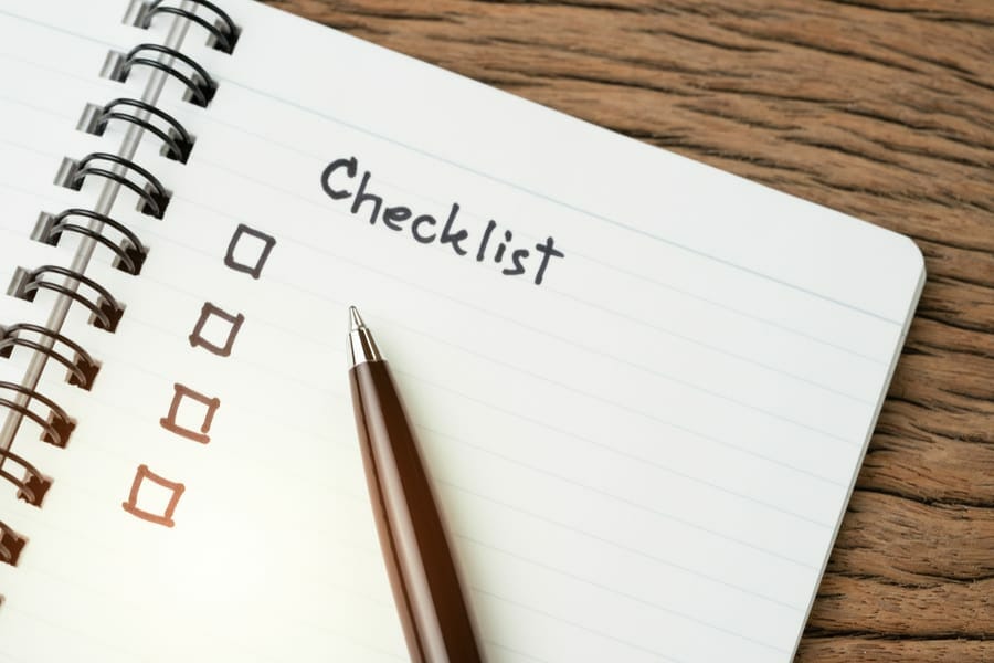 Checklist, to do list, prioritize or reminder for project plan, selective focus on pen with handwriting headline the word Checklist and check box on small notepad on wood table.
