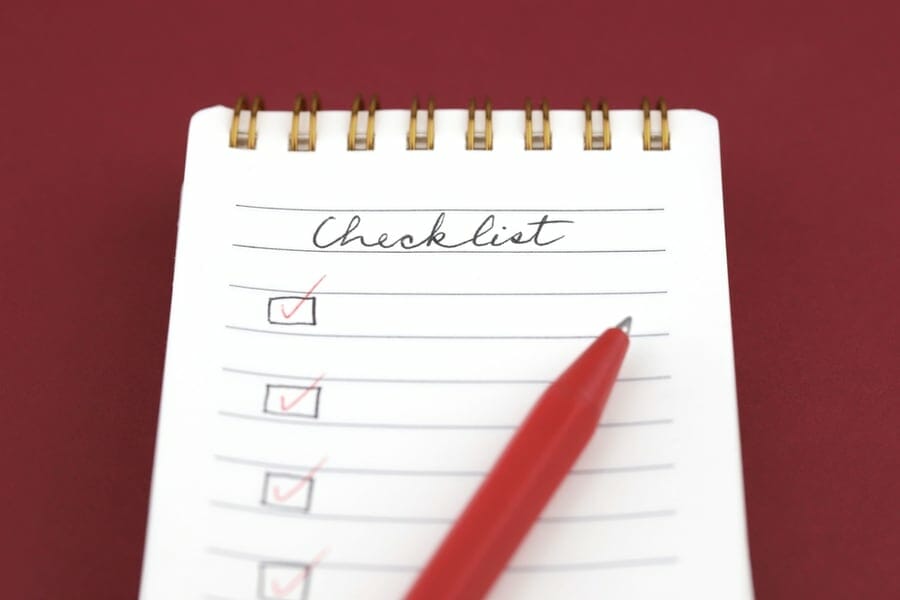 Red pen marking on checklist box in a spiral notepad on red background.