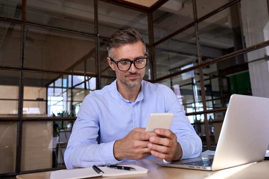 businessman holding mobile phone with laptop at desk office
