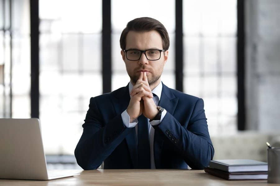 man with glasses in formal suit sitting at work desk