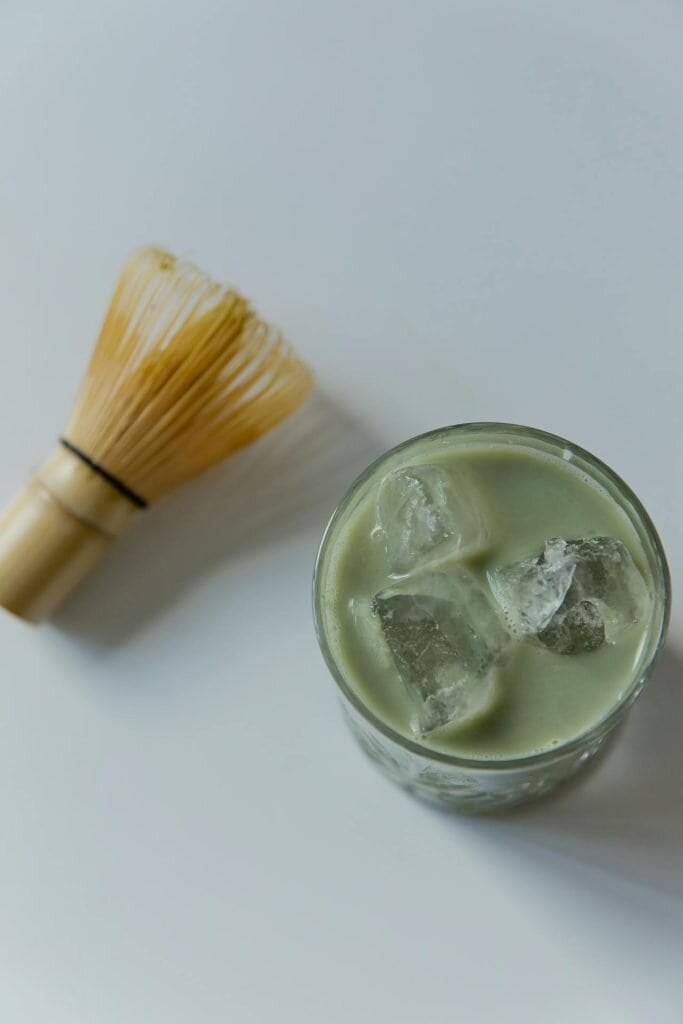 A glass of iced kratom drink and bamboo whisk on a white surface