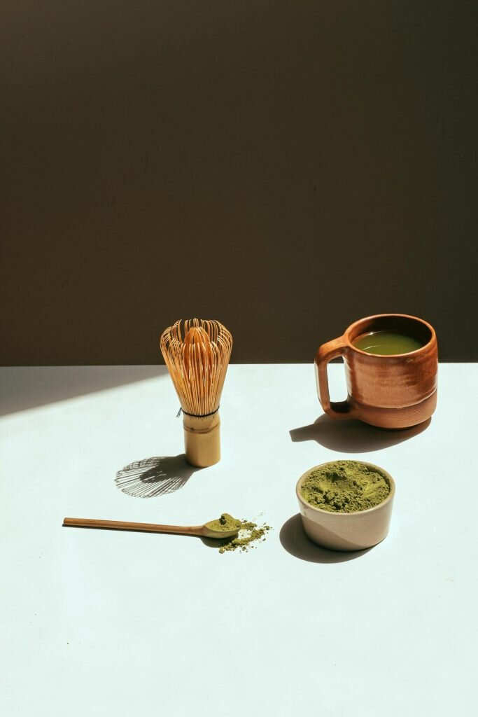 A bamboo whisk, kratom powder, and kratom drink arranged on a white surface